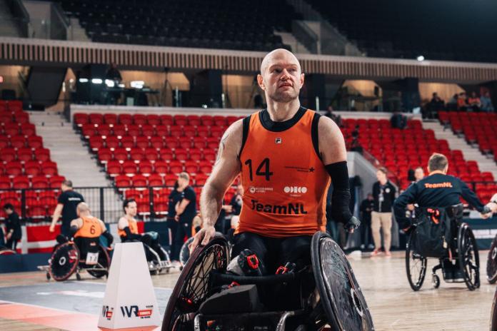 A male wheelchair rugby player wearing an orange jersey is exiting the court during competition
